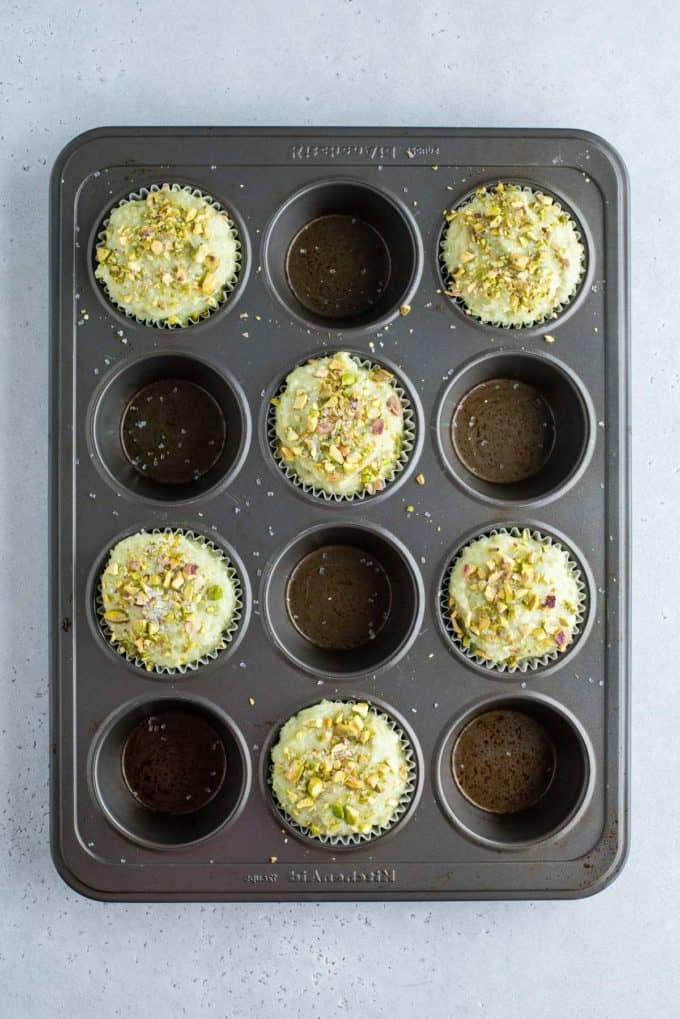Muffin al Pistacchio 5 Pistachio muffin batter filled in every other hole of a muffin tin.