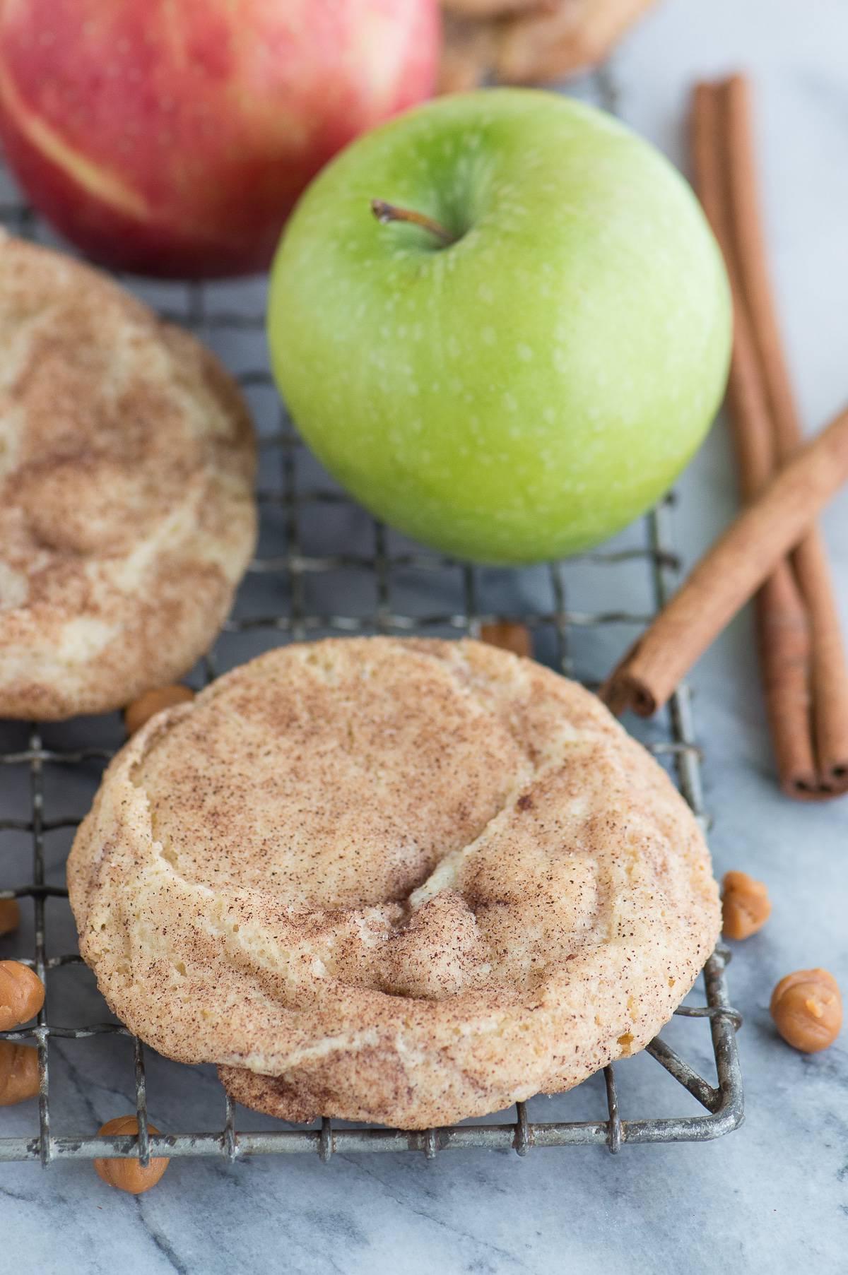 Biscotto snickerdoodle alla mela caramellata su una griglia di raffreddamento con caramelle, bastoncini di cannella e una mela sullo sfondo
