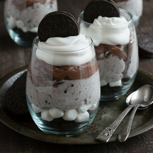 Due bicchieri di parfait al cioccolato, cheesecake e Oreo, con cucchiaini su un vassoio metallico