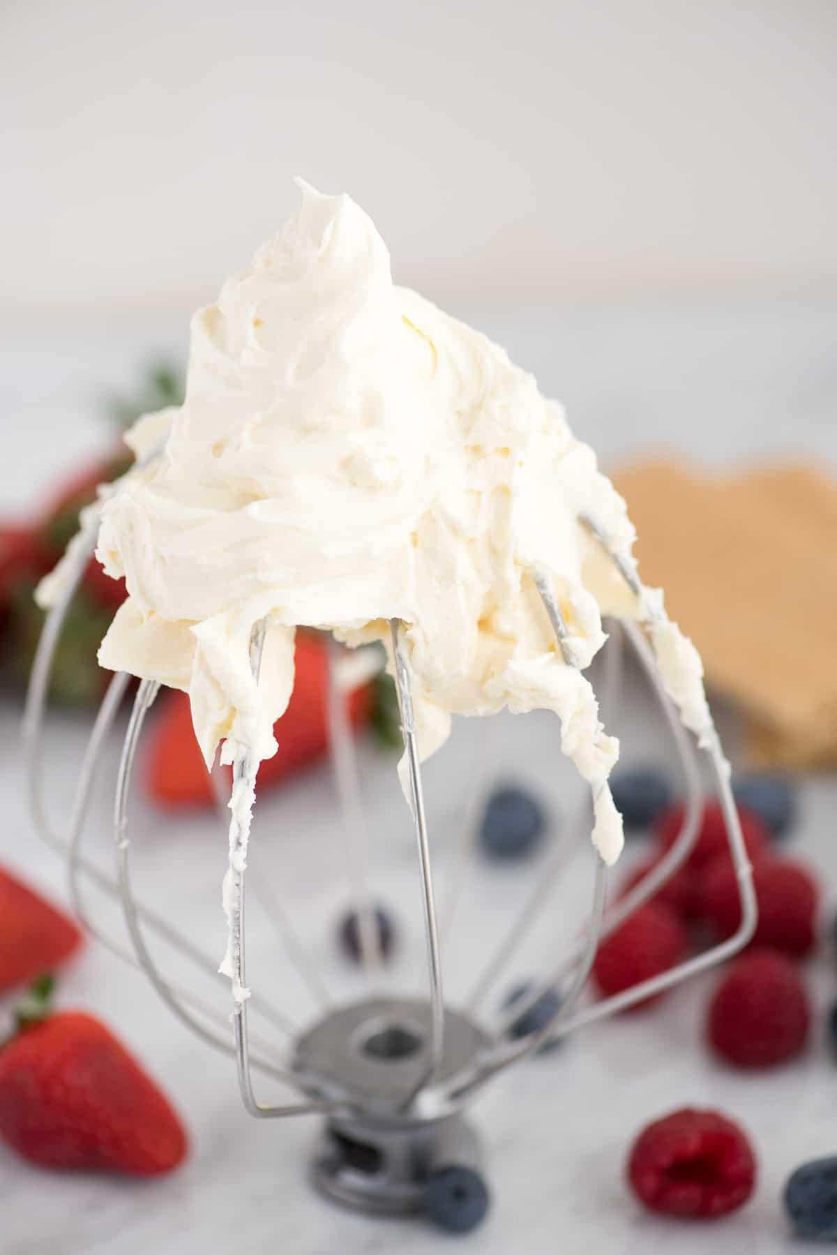 Frusta KitchenAid con panna montata al cheesecake e frutti di bosco sullo sfondo