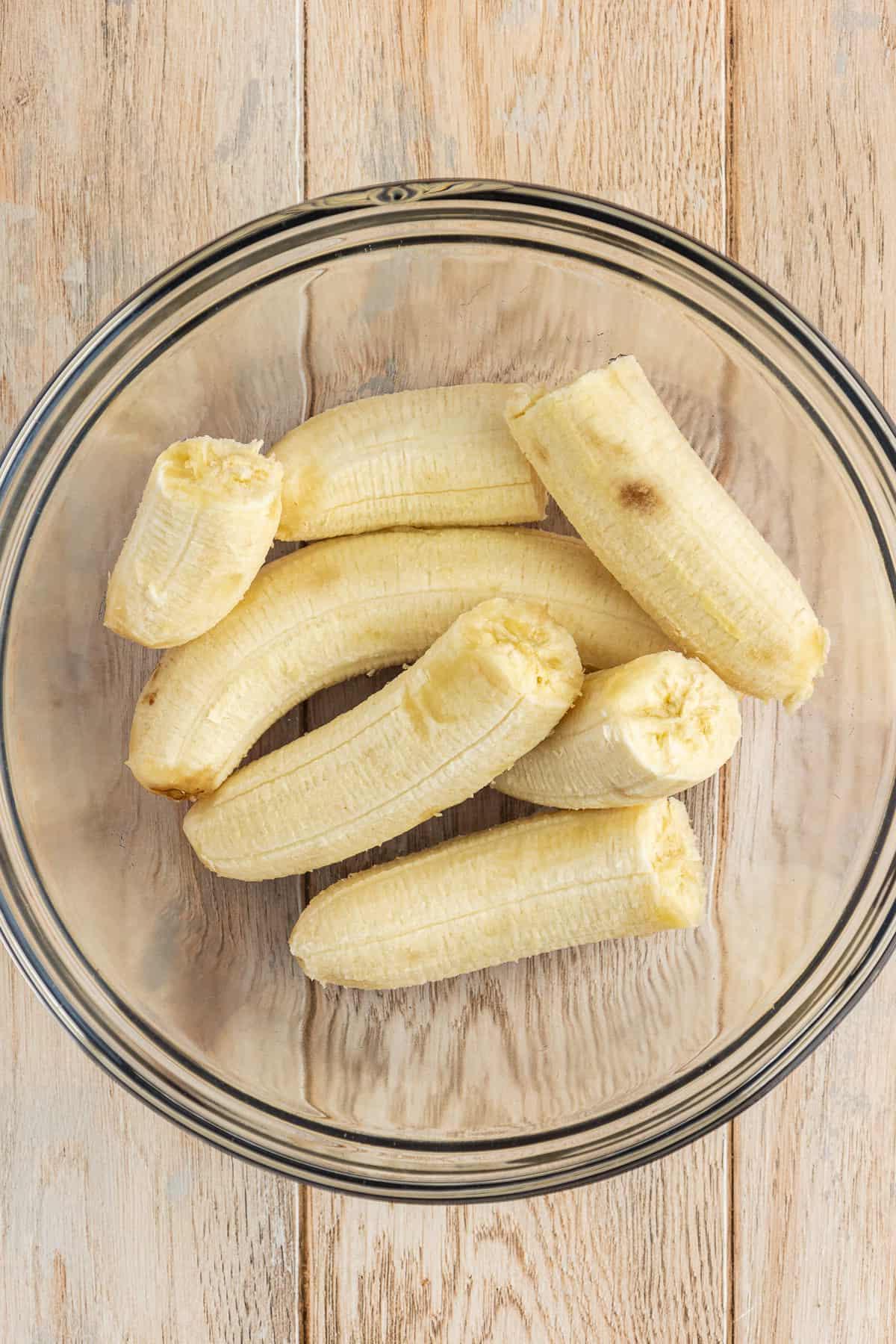 Una ciotola di vetro piena di metà di banane su una superficie di legno