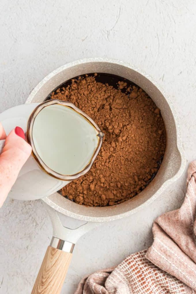 Ingredienti liquidi per la torta Texana in una casseruola con acqua versata e un panno da cucina color cuoio a sinistra