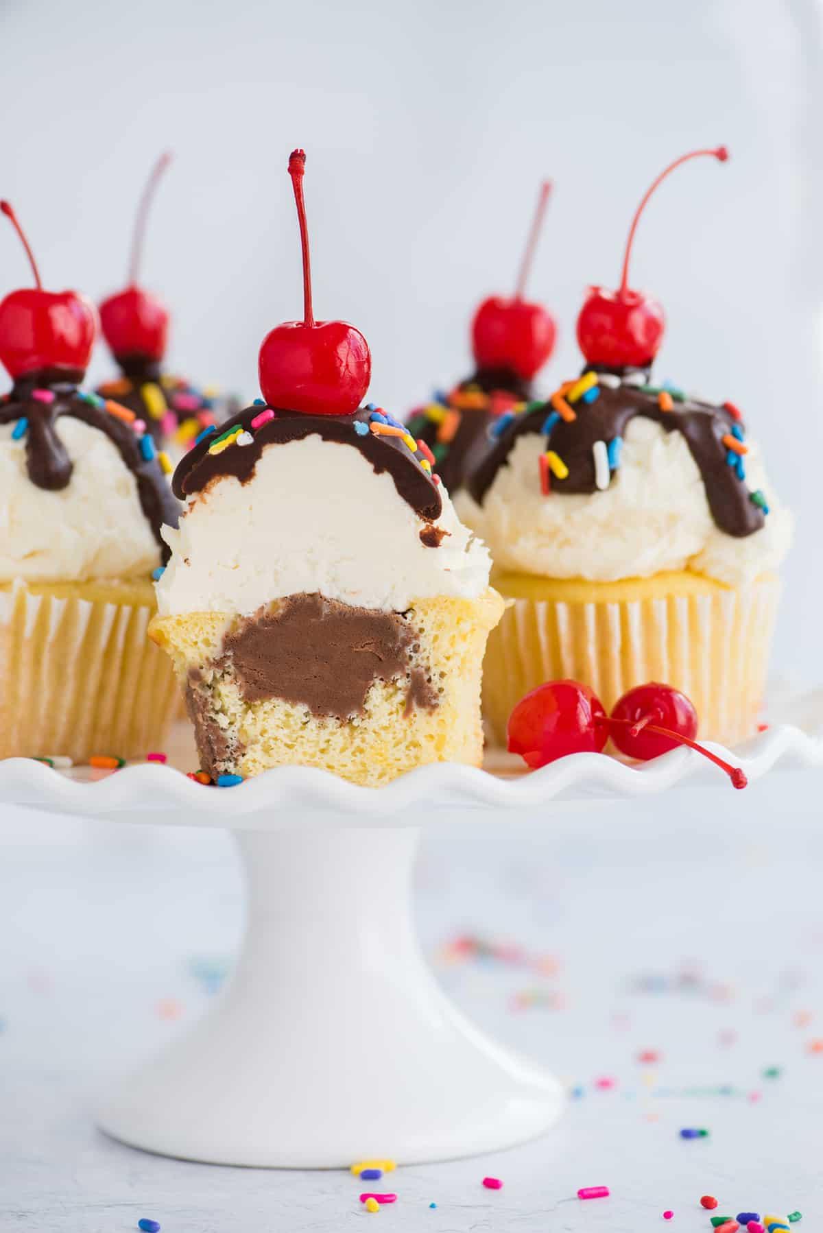 ice cream cupcakes with one cupcake cut in half showing chocolate ice cream center displayed on white cake stand on white background