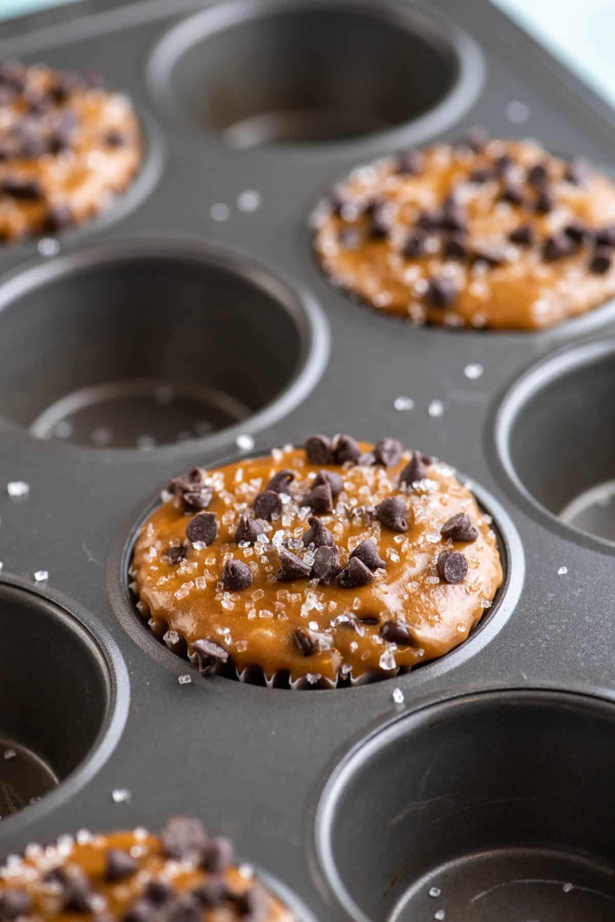 Muffin al Cappuccino e Gocce 6 impasto di muffin al cappuccino con gocce di cioccolato che riempie un foro sì e uno no di una teglia per muffin, condito con mini gocce di cioccolato e spolverato di zucchero semolato grosso