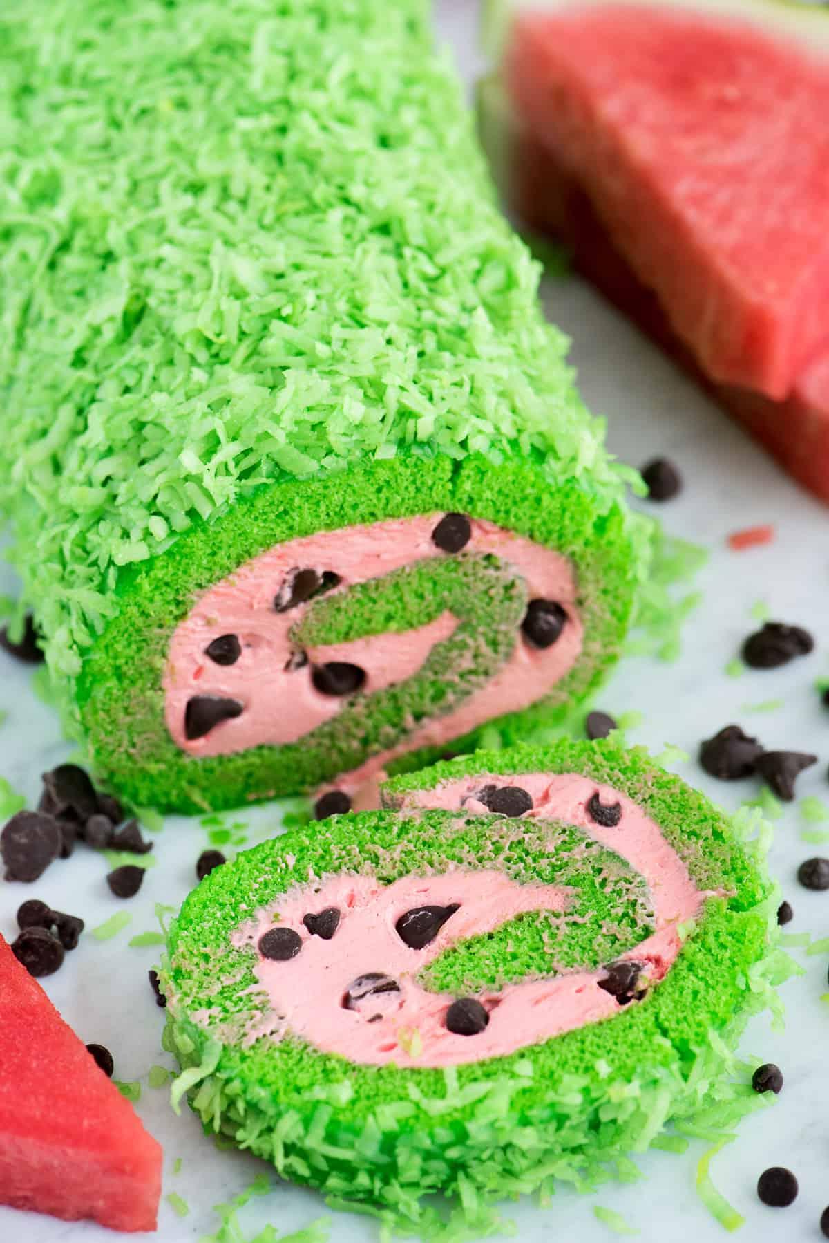 Questa torta rotolo anguria estiva sarebbe così divertente da includere in una festa a tema anguria! Una torta rotolo anguria già completata, con la sua caratteristica colorazione verde all'esterno e il ripieno rosso/rosa con i semi di cioccolato, pronta per essere servita o fotografata.