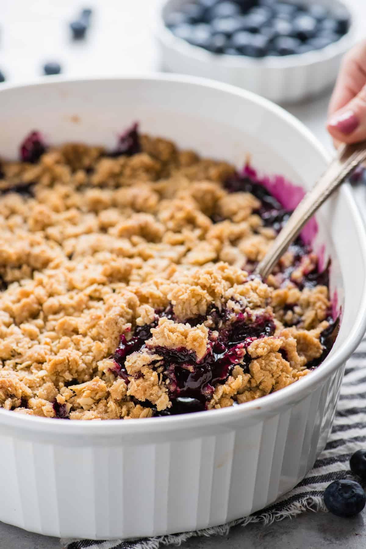 Crumble ai mirtilli in una teglia bianca con un cucchiaio di metallo