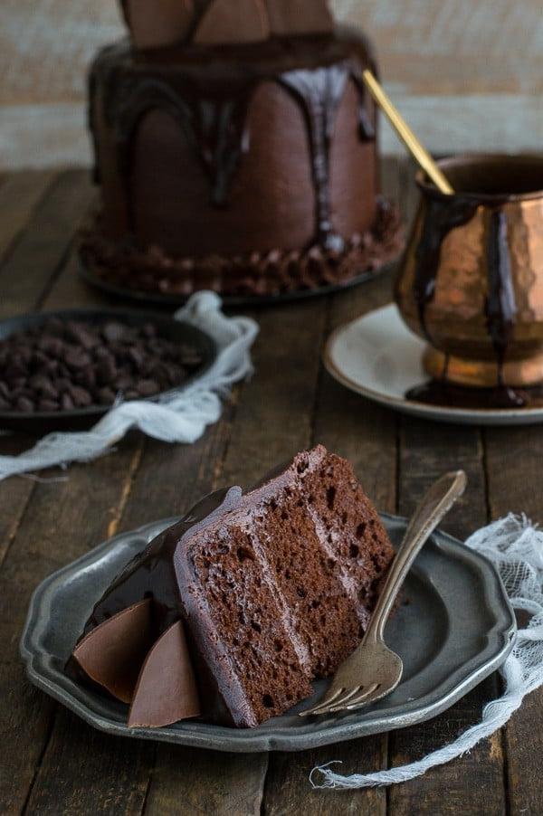 Una fetta di Torta al Cioccolato Cioccolato con ganache al cioccolato e scaglie di cioccolato su un piccolo piatto da portata.