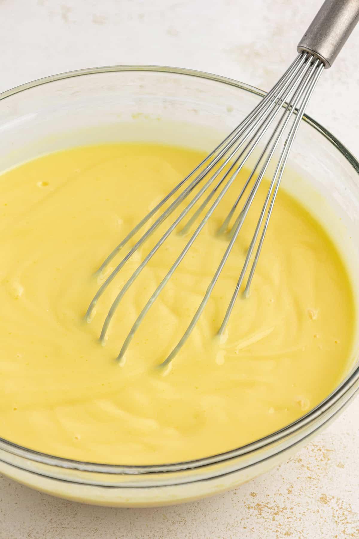 Budino istantaneo alla vaniglia mescolato in una ciotola di vetro trasparente con una frusta
