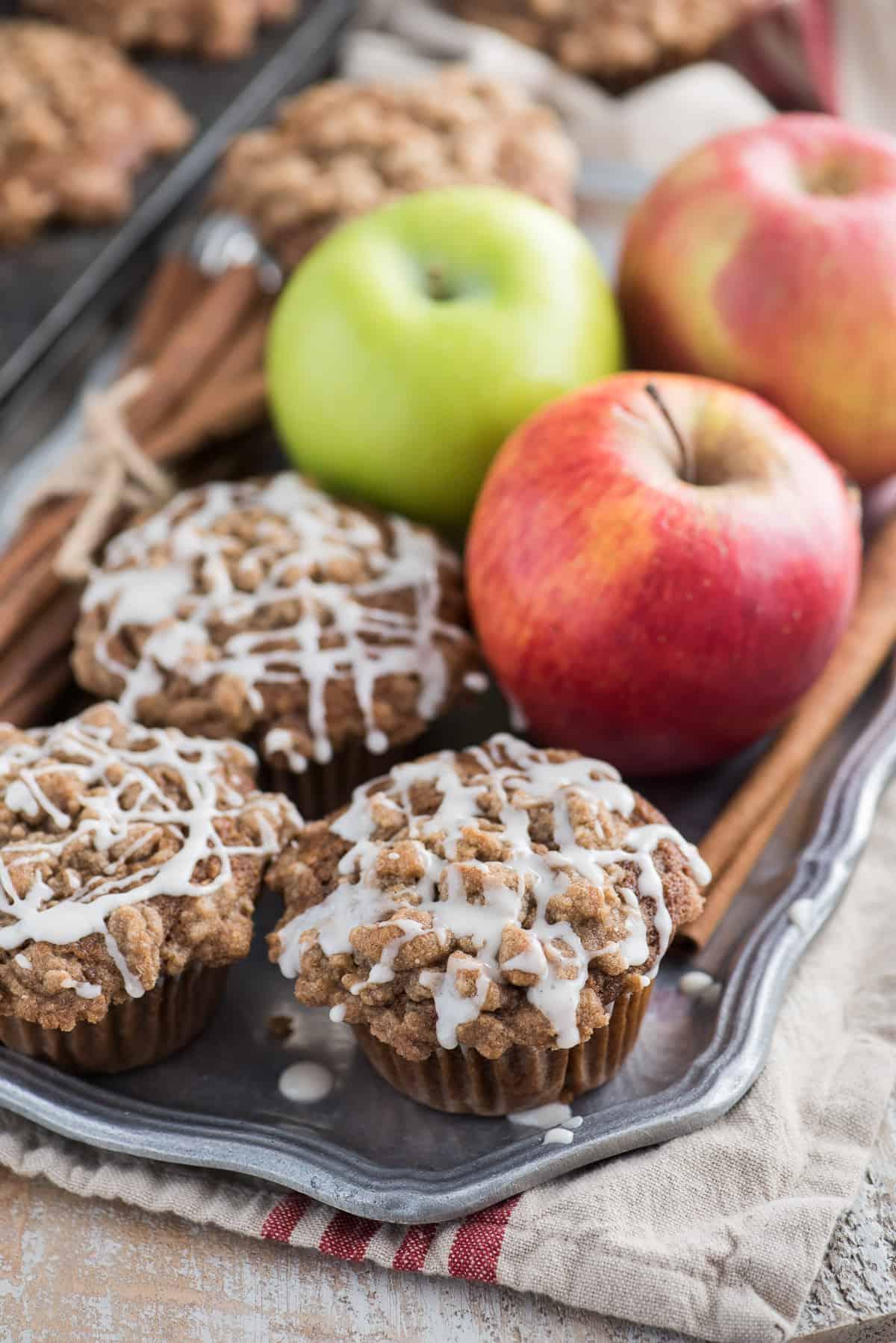 Muffin speziati alla salsa di mele con crumble e glassa bianca su un piatto di metallo, con mele sullo sfondo