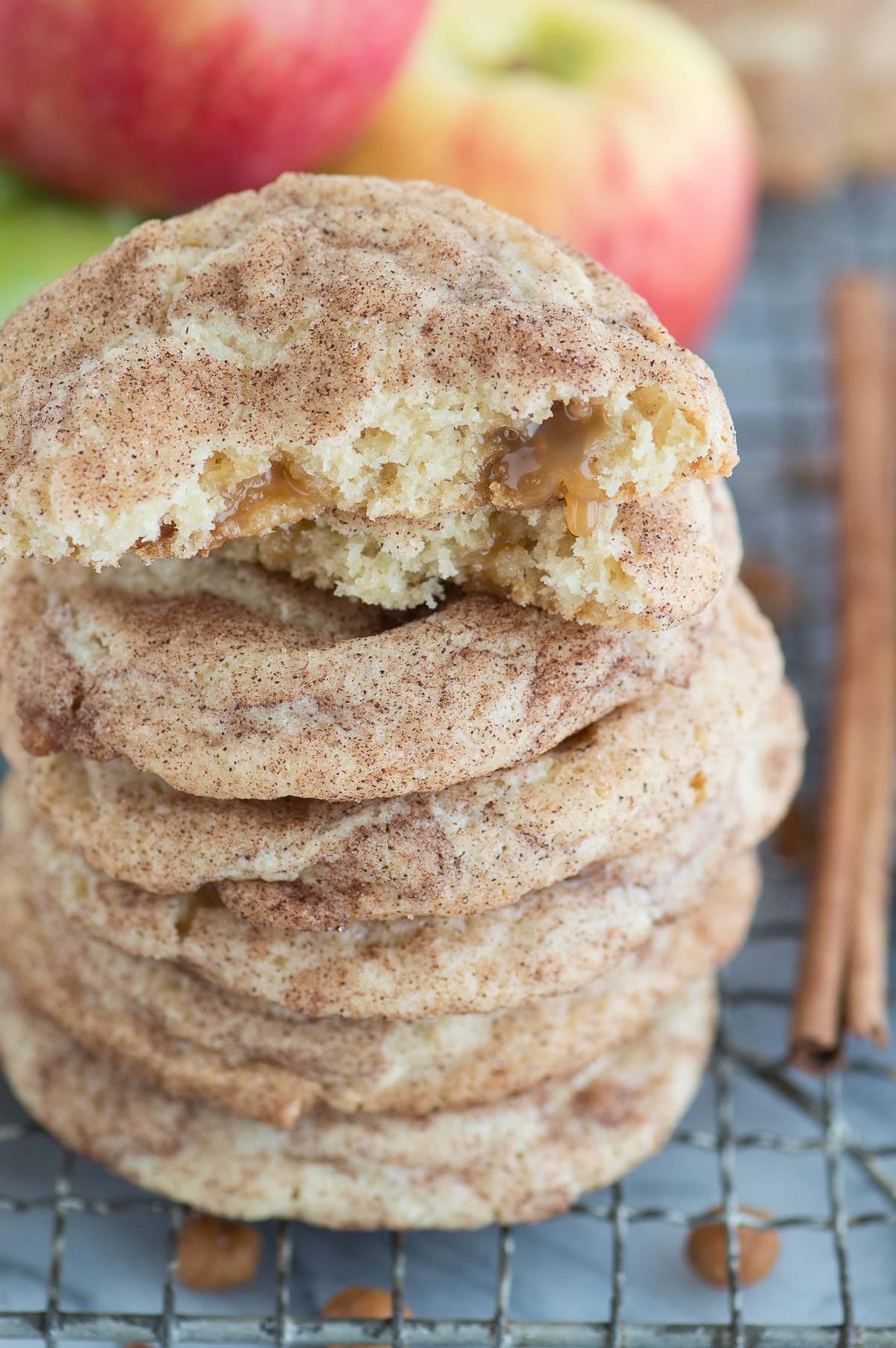 Biscotti snickerdoodle alle mele caramellate impilati su una griglia di raffreddamento metallica con mele sullo sfondo