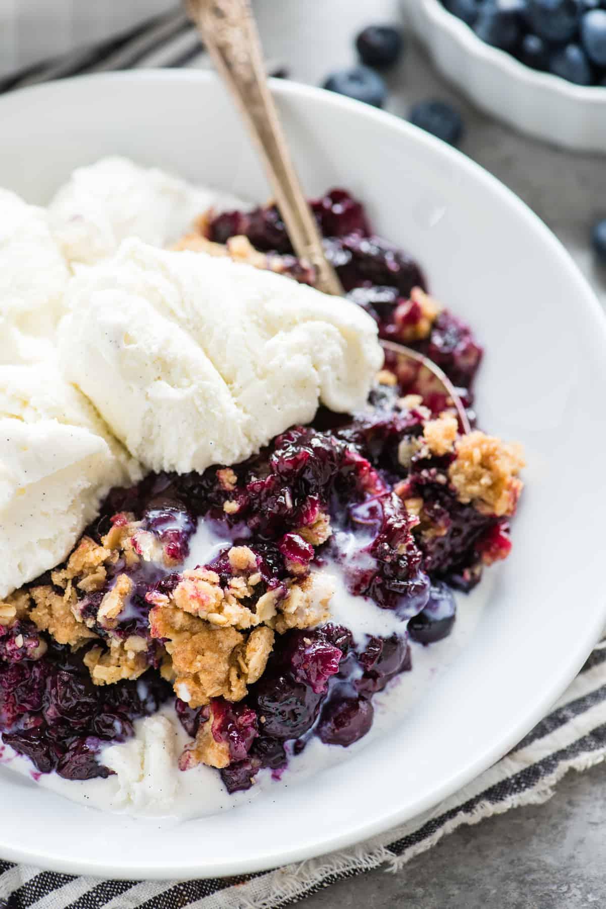 Crumble ai mirtilli in una teglia bianca con un cucchiaio di metallo
