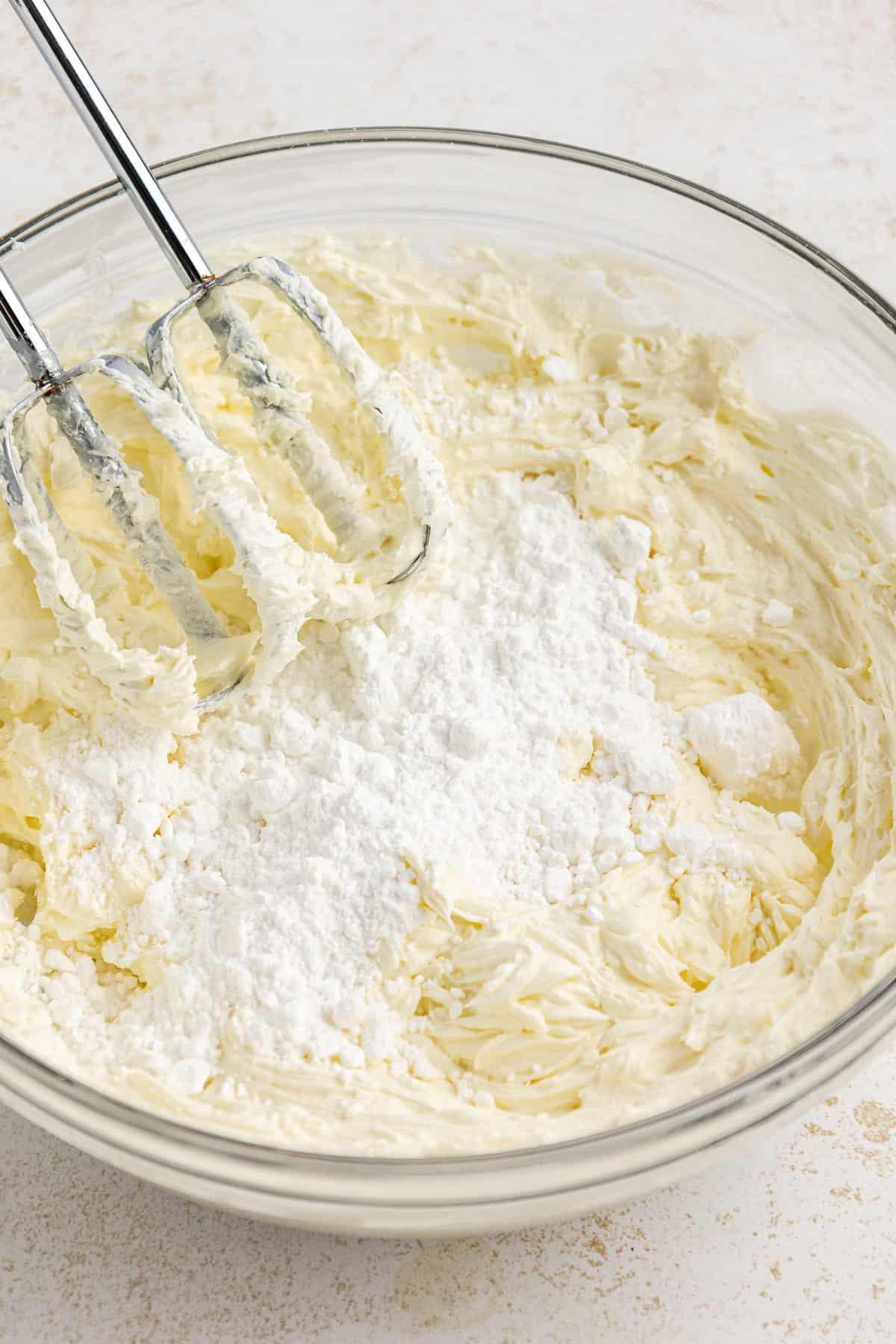 Una miscela di crema di formaggio, burro e zucchero a velo viene sbattuta in una grande ciotola di vetro trasparente con un mixer elettrico