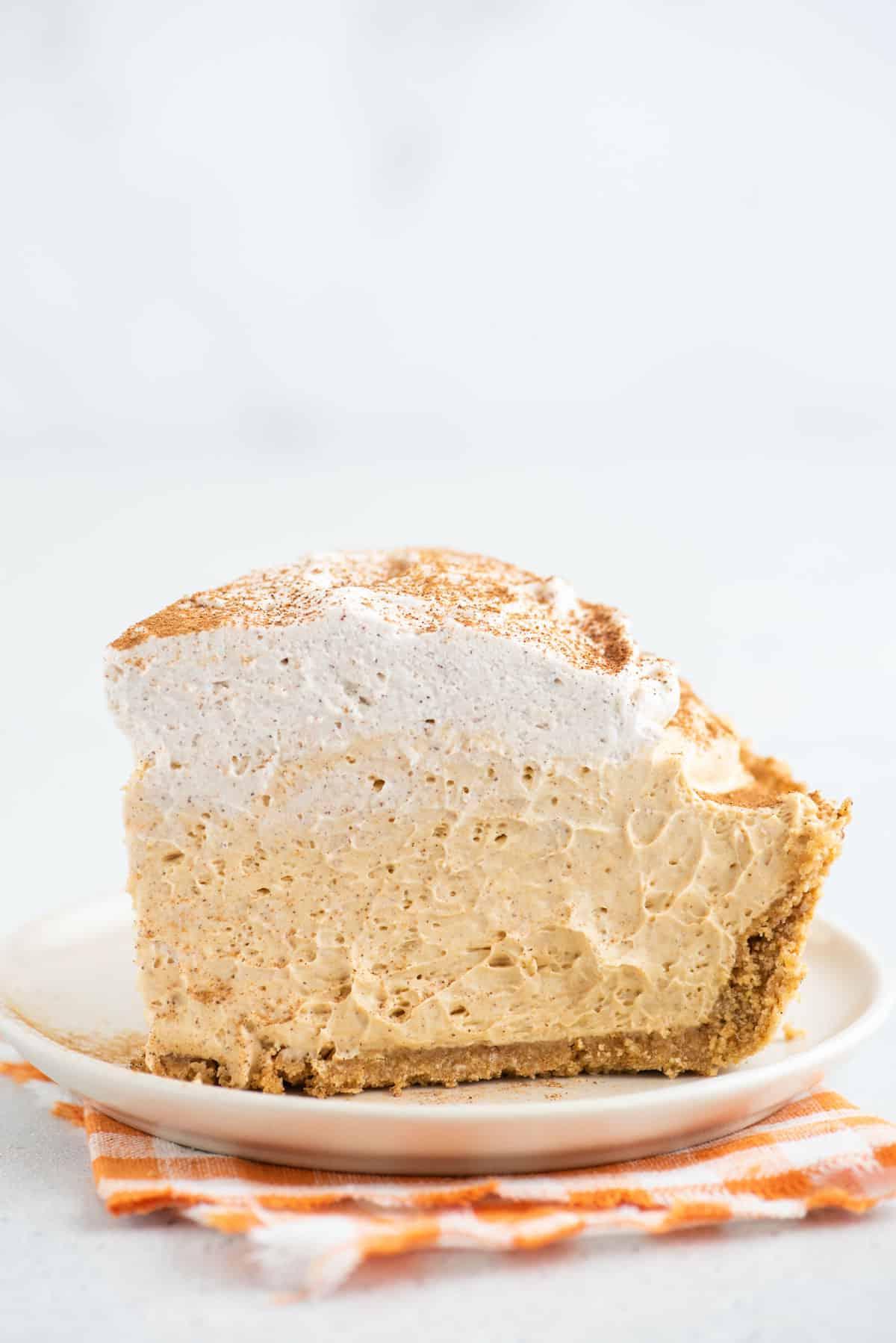 Una fetta alta di torta di zucca senza cottura è adagiata su un piatto bianco.