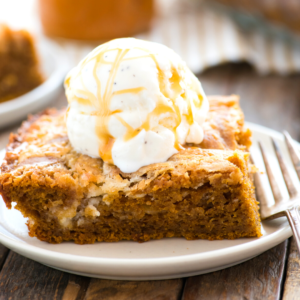 Torta Terremoto alla Zucca 7 Una fetta di torta terremoto alla zucca umida e dorata con una pallina di gelato alla vaniglia irrorata di salsa al caramello, servita su un piatto bianco con una forchetta.