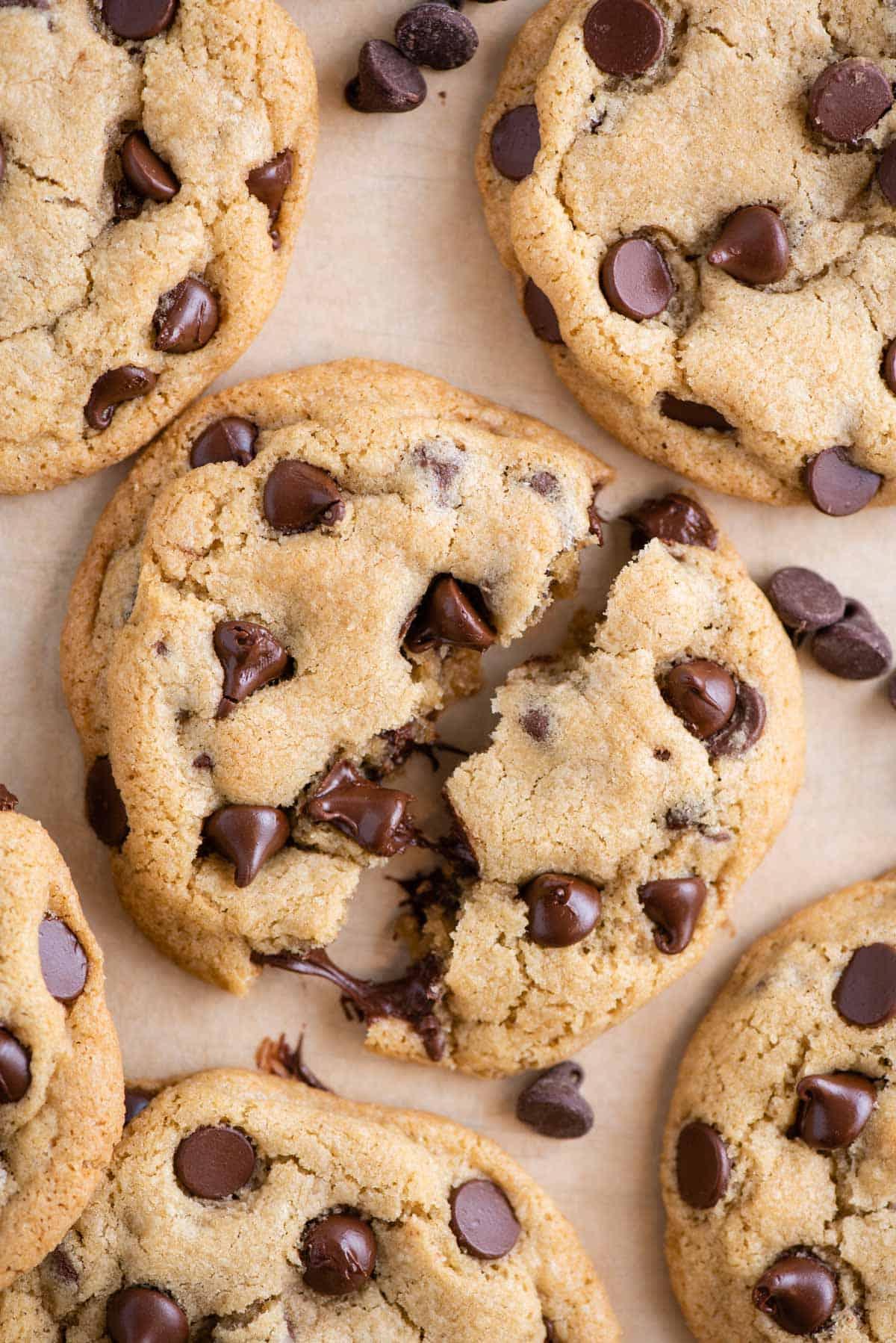 Visuale dall'alto di biscotti con gocce di cioccolato su carta forno, con uno spezzato a metà per mostrare le gocce di cioccolato fondenti