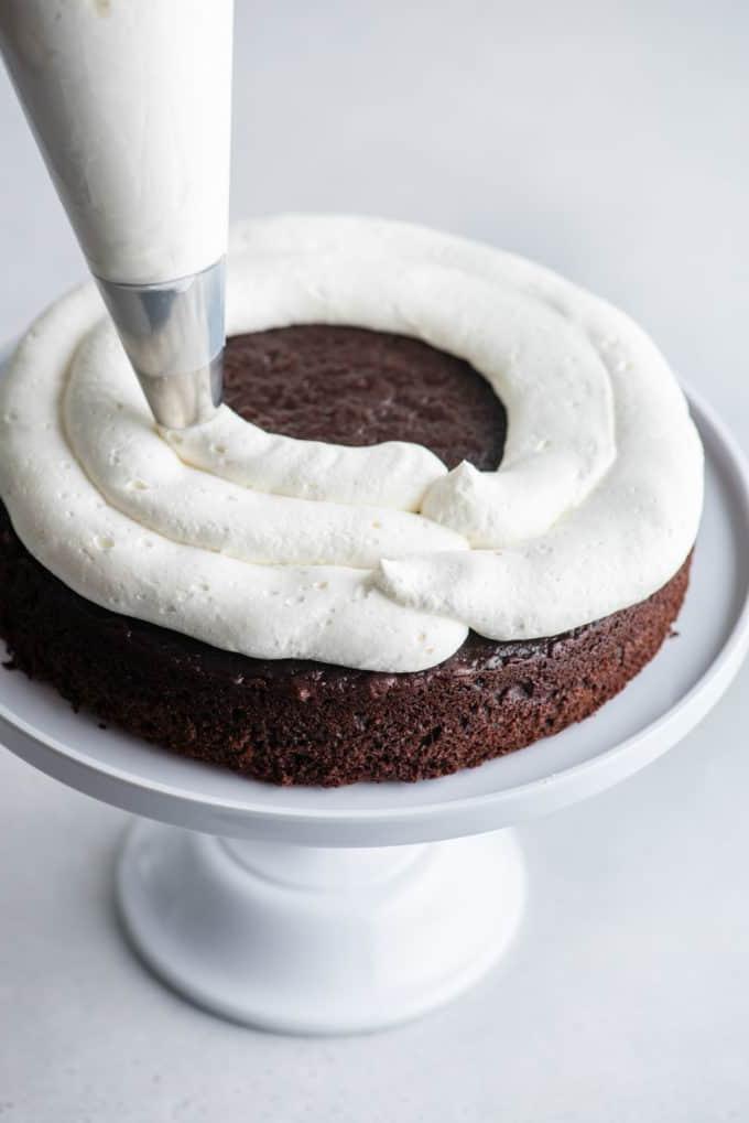 Uno strato di pan di Spagna al cioccolato su un'alzatina bianca con la panna montata stabilizzata che viene messa sopra con una sac à poche