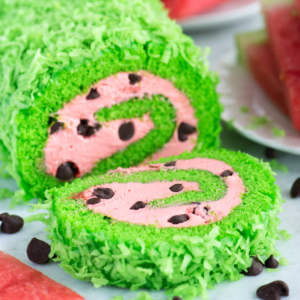 Rotolo all'Anguria 6 Una deliziosa torta rotolo anguria decorata per sembrare un'anguria, con scaglie di cocco verde brillante all'esterno, ripieno rosa a spirale, e gocce di cioccolato che ricordano i semi.