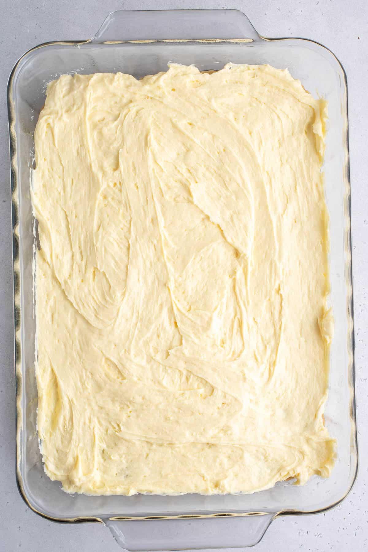 Una teglia trasparente con i primi due strati di brownies al budino di banana, lo strato blondie e lo strato di miscela di budino di banana
