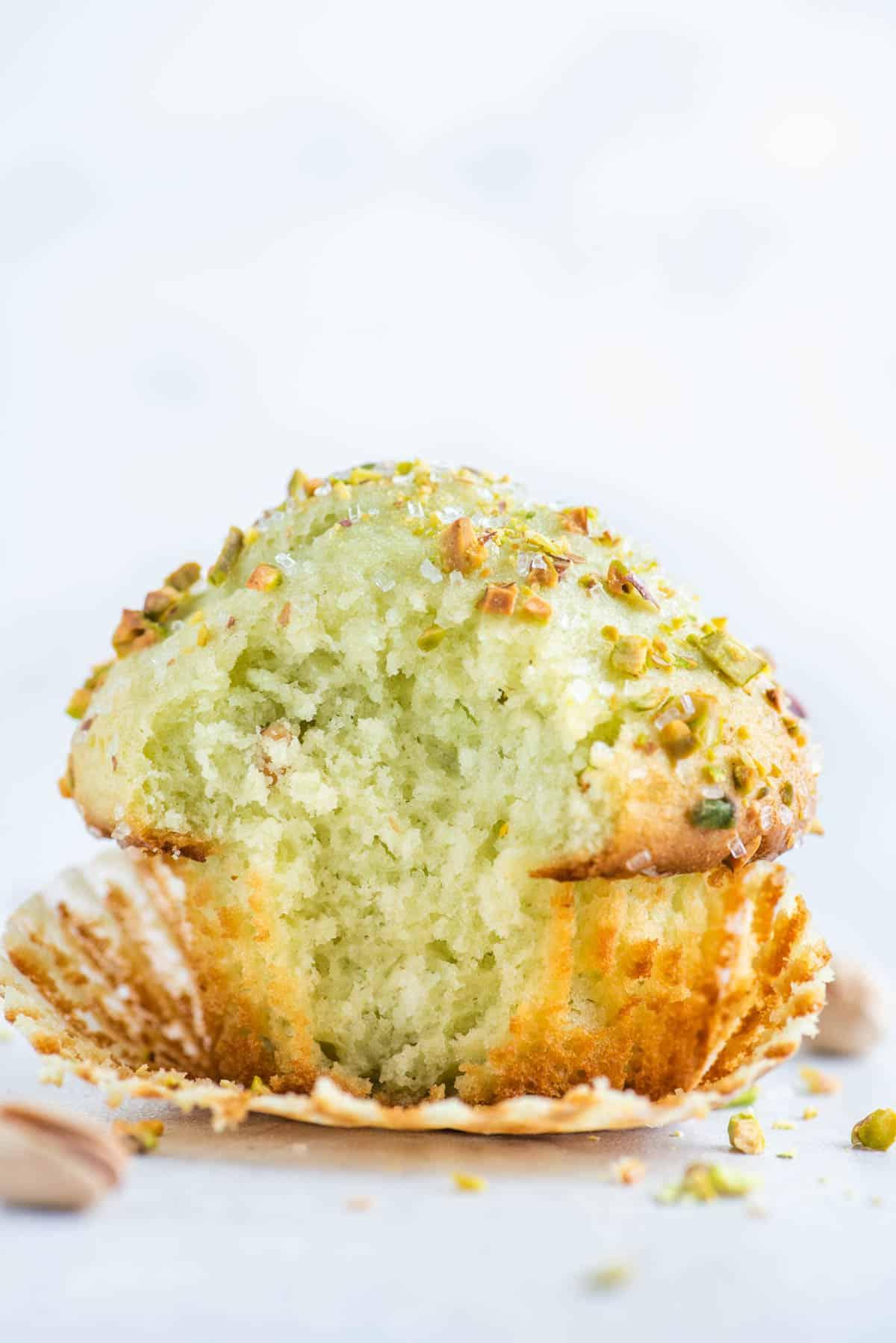 Muffin al Pistacchio 8 A pistachio muffin with the muffin paper partially pulled off and a bite taken out.