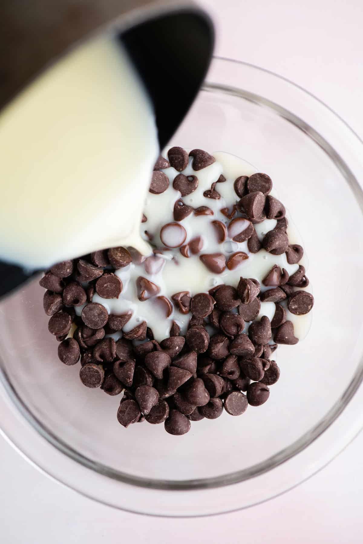 Una miscela di panna fresca e zucchero versata su una ciotola di vetro di gocce di cioccolato per fare la salsa hot fudge fatta in casa