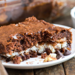 Torta Terremoto 8 Un primo piano di un brownie al cioccolato ispirato alla torta terremoto con un ripieno bianco cremoso e gocce di cioccolato sparse, servito su un piatto bianco su una superficie di legno rustico.