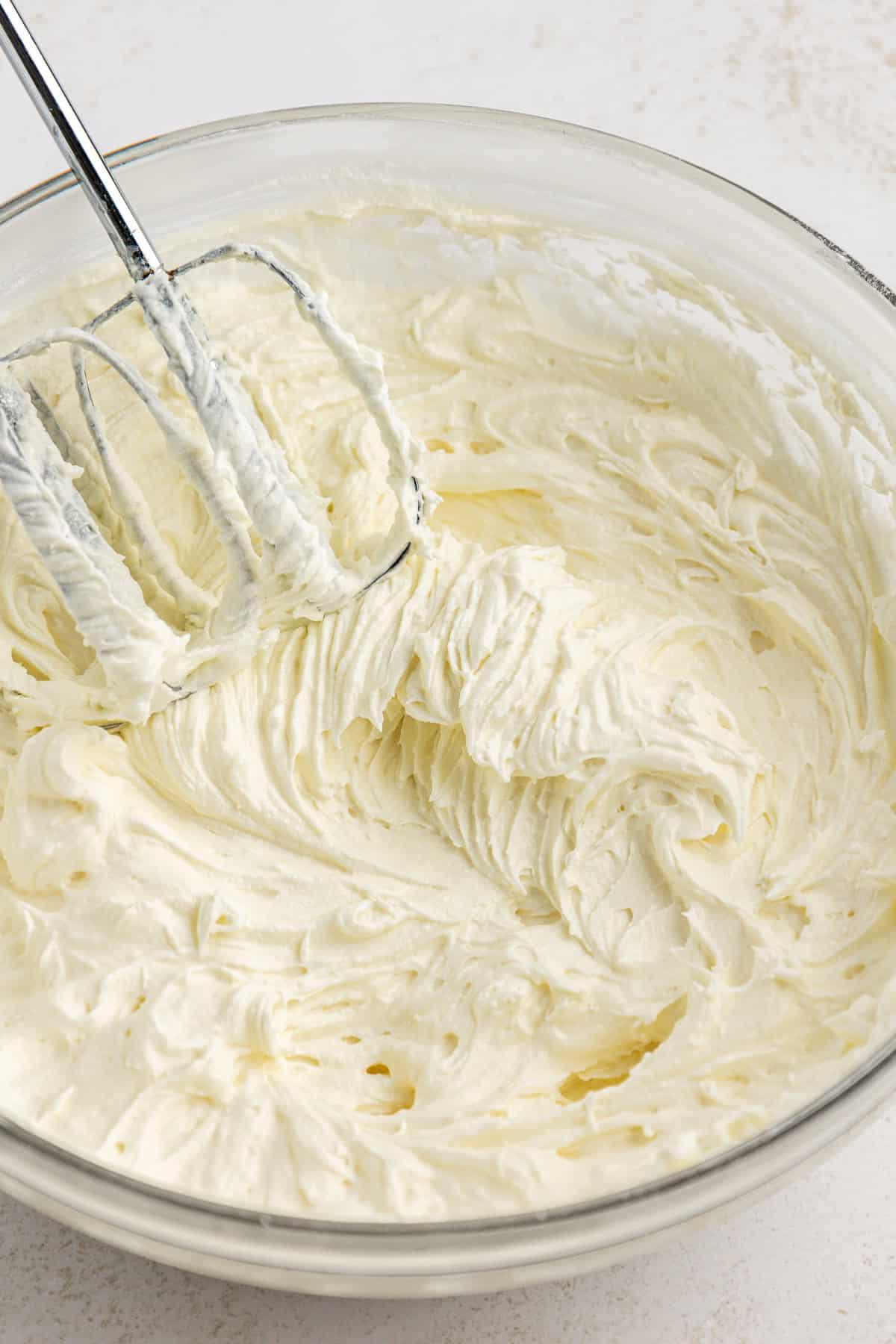 Crema di formaggio, burro e zucchero a velo mescolati in una ciotola di vetro trasparente con un mixer elettrico