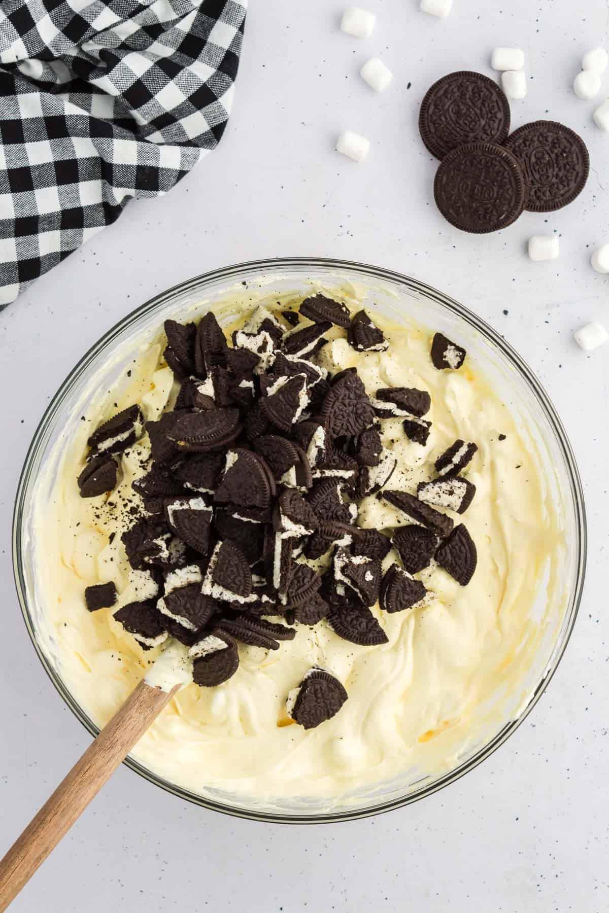 Miscela di fluff di Oreo sormontata da Oreo tritati, circondata da Oreo, mini marshmallow e un panno da cucina a scacchi bianchi e neri