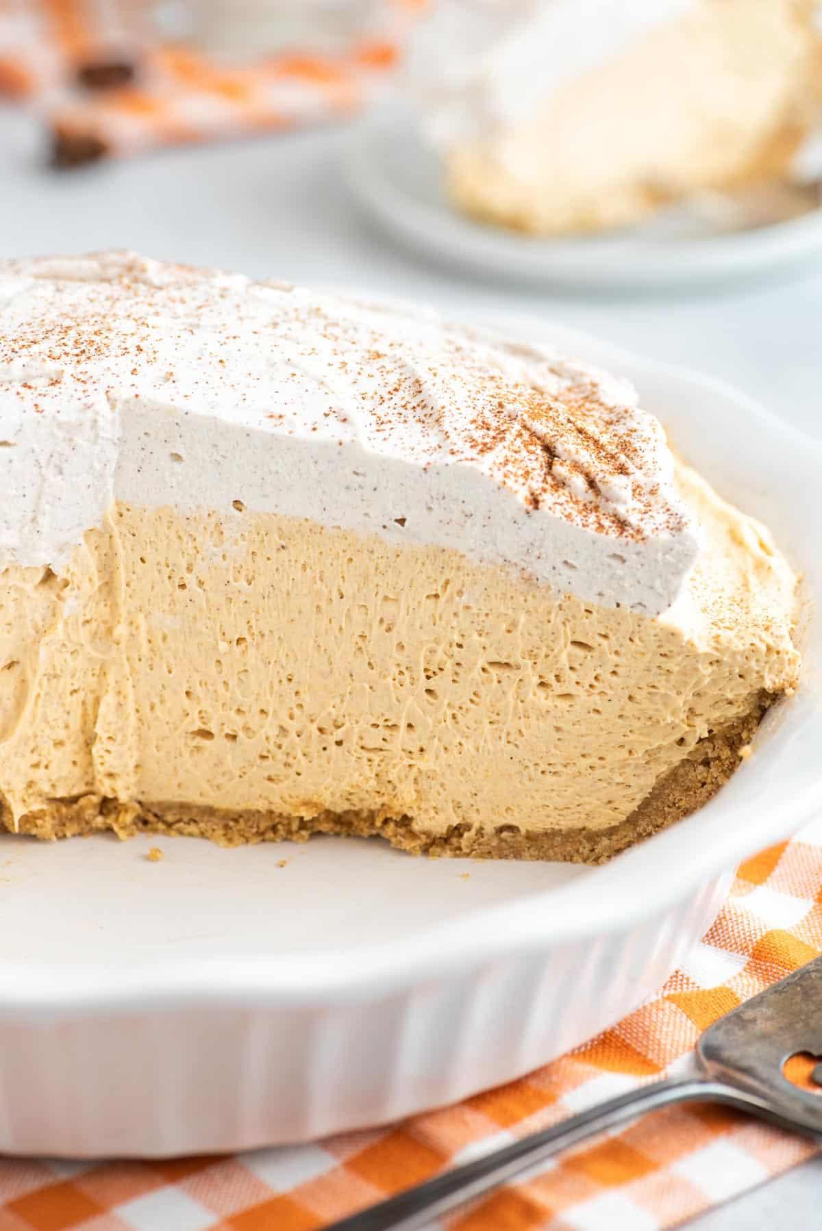 Un pezzo leggero e cremoso di torta di zucca senza cottura adagiato su un piatto da dessert bianco.