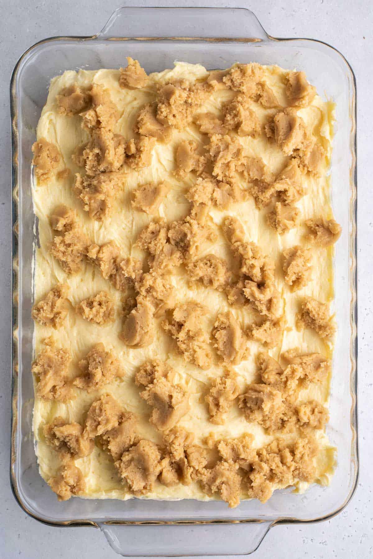 Una teglia trasparente con gli strati di brownies al budino di banana, lo strato blondie, la miscela di budino di banana e un altro strato di miscela blondie prima della cottura