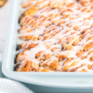 A close-up of a cinnamon roll casserole showcases golden-brown rolls packed together, generously drizzled with white icing. The soft, fluffy breakfast casserole looks irresistibly sweet and ready to enjoy.