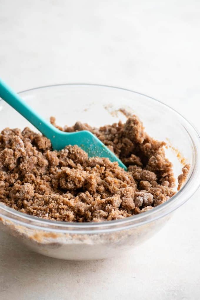 Topping di crumble per torta al caffè in una ciotola di vetro trasparente con una spatola verde acqua al suo interno