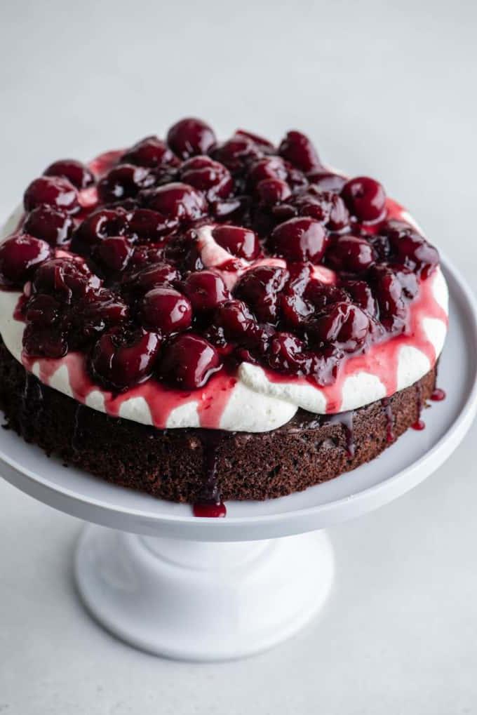 Uno strato di pan di Spagna al cioccolato su un'alzatina bianca con la panna montata stabilizzata sopra e una salsa di ciliegie sopra, con un altro strato di pan di Spagna al cioccolato sopra