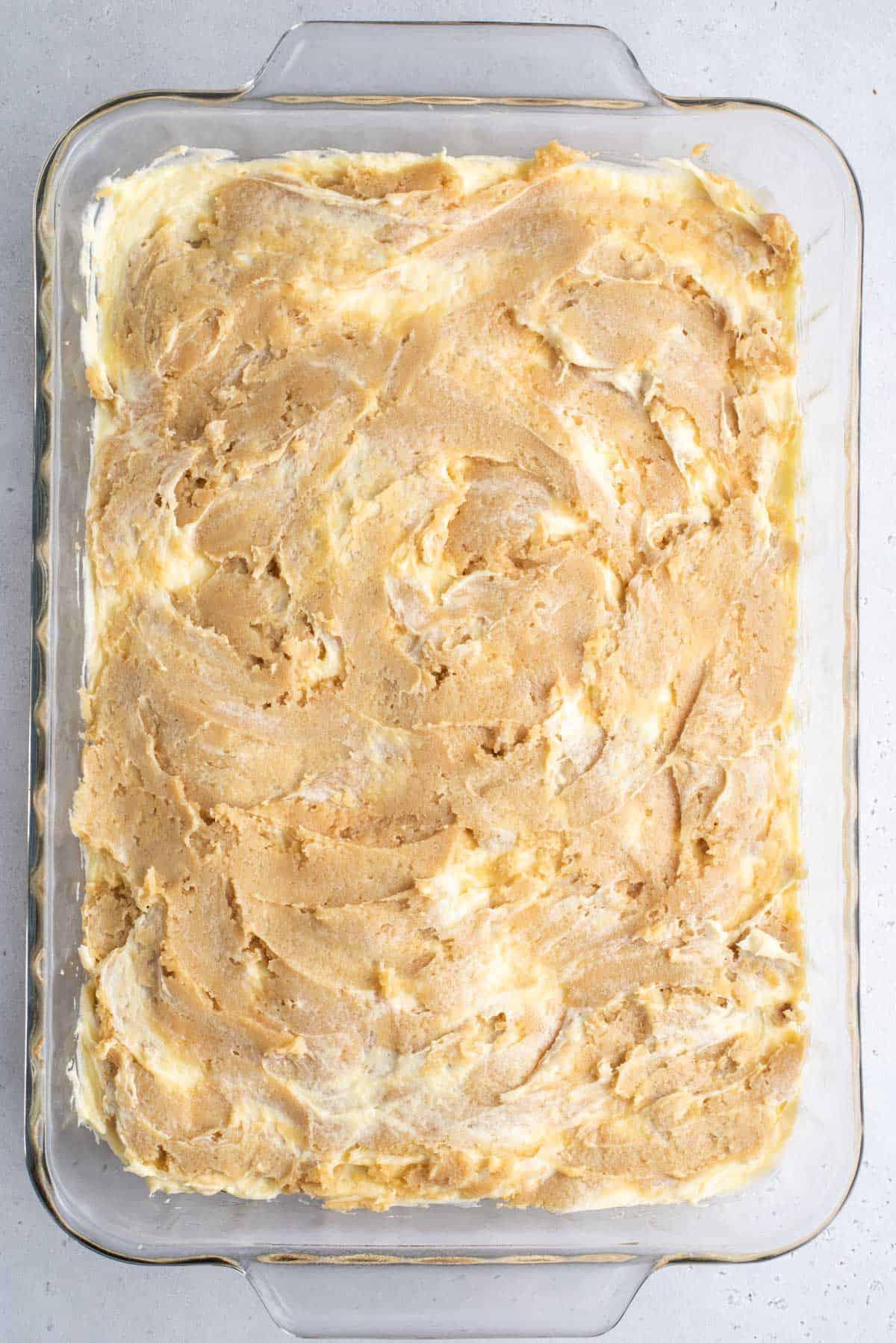 Una teglia trasparente con gli strati di brownies al budino di banana, lo strato blondie, la miscela di budino di banana e un altro strato di miscela blondie prima della cottura