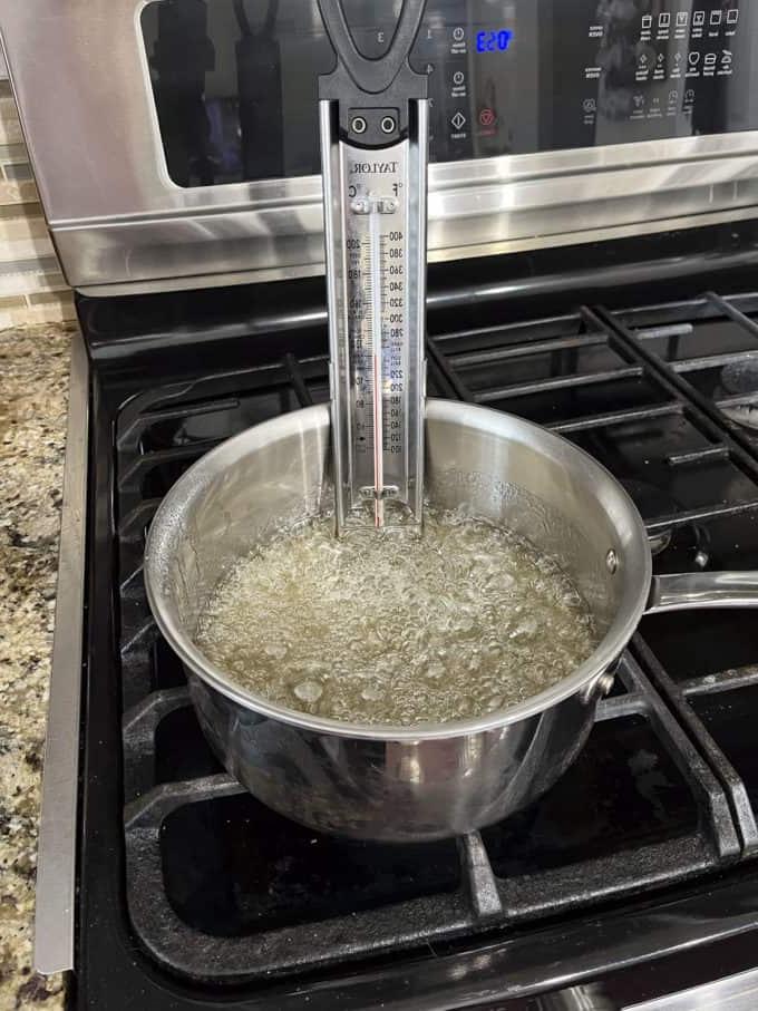 Una pentola sul fornello con zucchero semolato, acqua e sciroppo di mais che cuociono e un termometro per dolci attaccato al lato