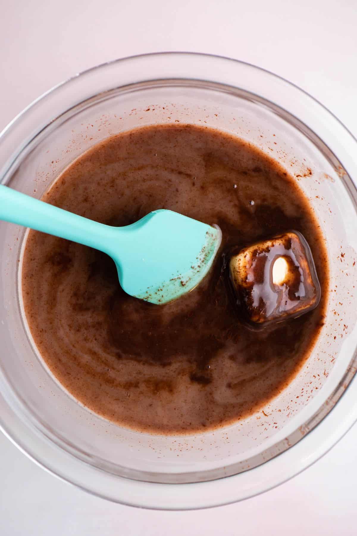Salsa hot fudge fatta in una ciotola di vetro mescolando il burro con il resto degli ingredienti usando una spatola color verde acqua