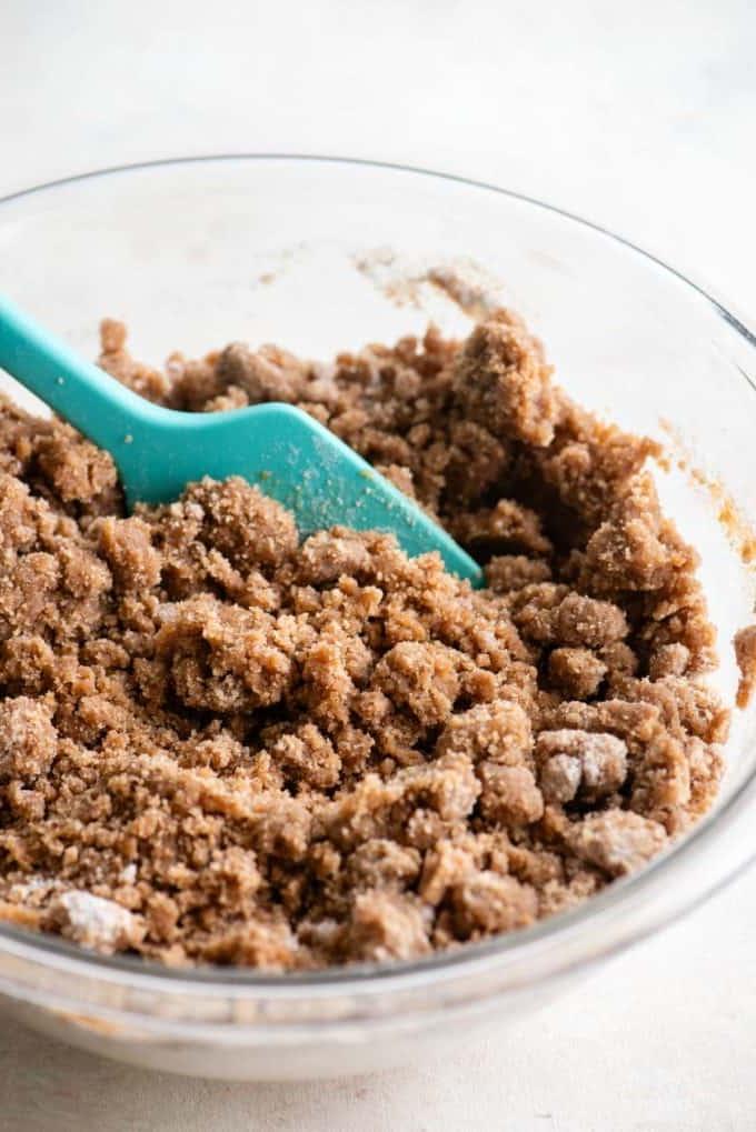 Primo piano del topping di crumble per torta al caffè in una ciotola di vetro trasparente con una spatola verde acqua al suo interno