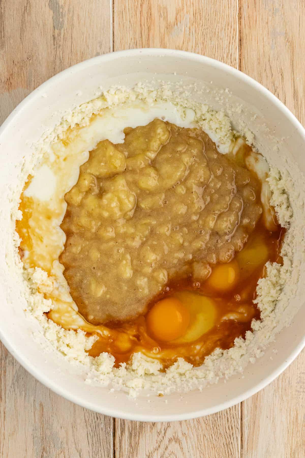 Una ciotola bianca con una miscela di burro e zucchero, banane schiacciate, uova, latticello ed estratto di vaniglia non ancora mescolati