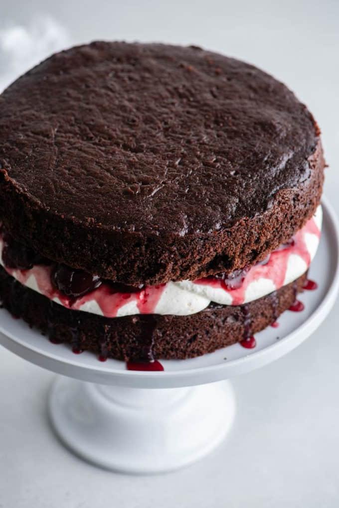 Uno strato di pan di Spagna al cioccolato su un'alzatina bianca con la panna montata stabilizzata sopra e una salsa di ciliegie sopra, con un altro strato di pan di Spagna al cioccolato sopra