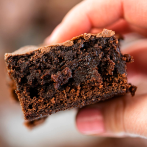 Trucchi per Brownie in Scatola 10 Primo piano di un brownie al cioccolato fudgy tenuto in mano, con la sua crosticina lucida e interna umida.