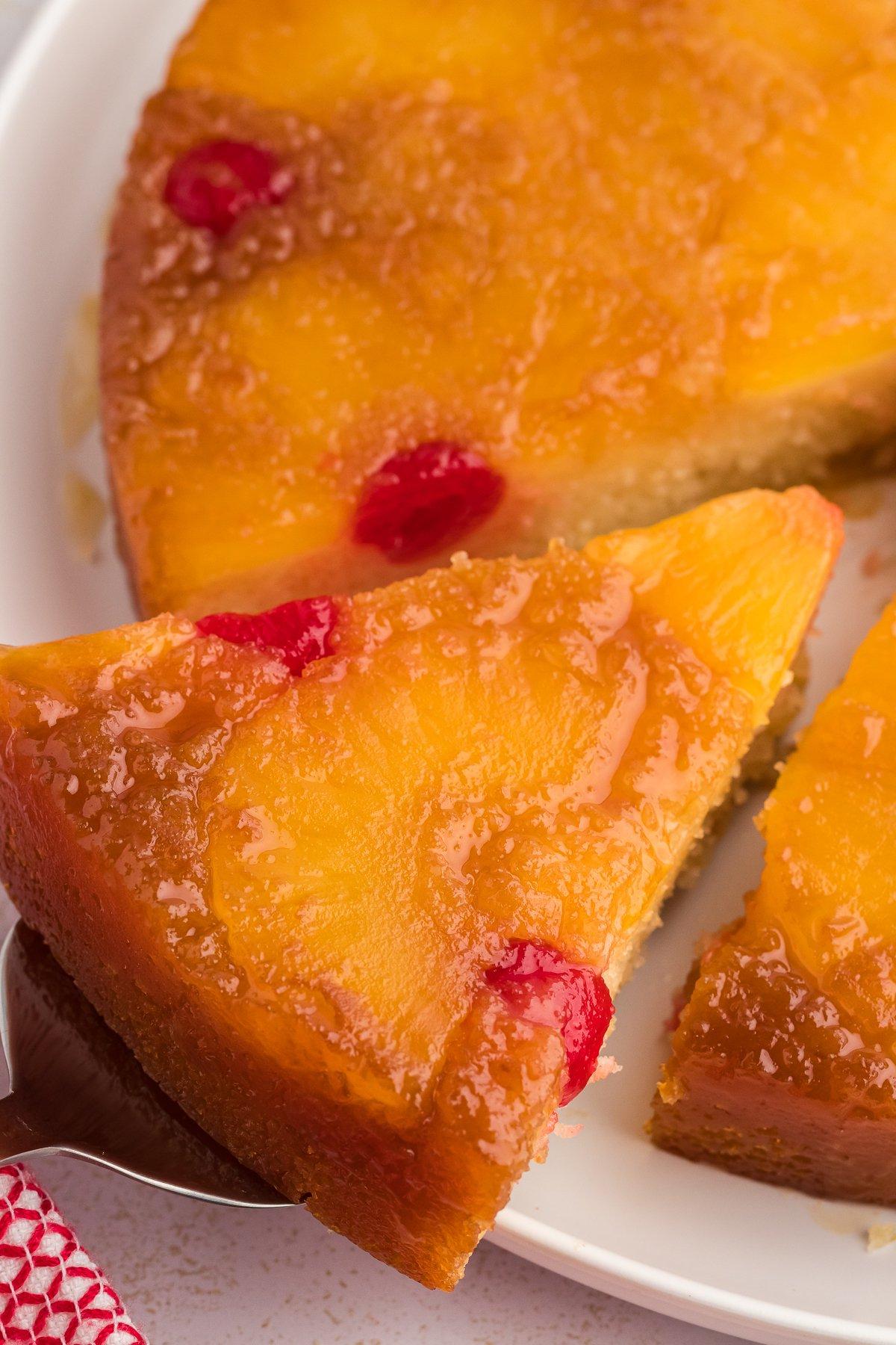 Primo piano di una fetta di torta rovesciata all'ananas che viene sollevata dal piatto, lontano dal resto della torta.
