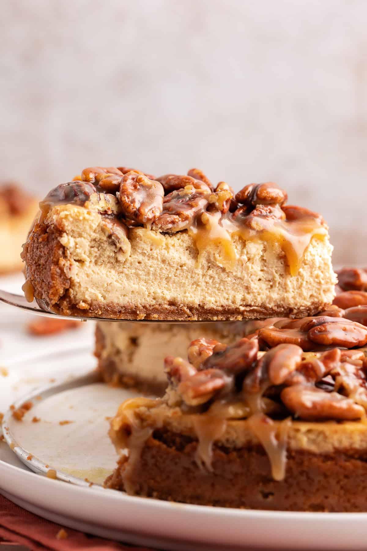 Vista laterale di una fetta di cheesecake alle noci pecan sollevata dal resto della cheesecake con una spatola da portata