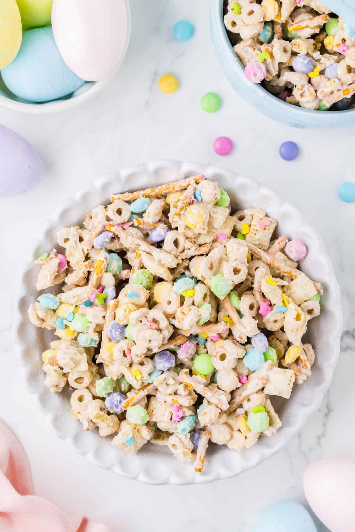 Una grande ciotola bianca di snack mix 'Bunny Bait' circondata da una ciotola più piccola di 'Bunny Bait' e una ciotola di uova di Pasqua