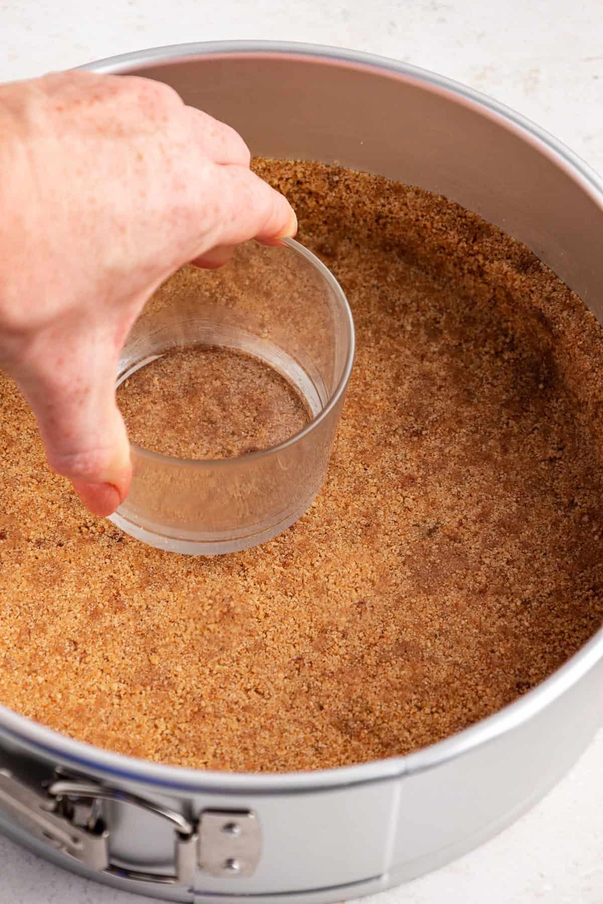 Base di biscotti graham pressata in una tortiera a cerniera con un bicchiere