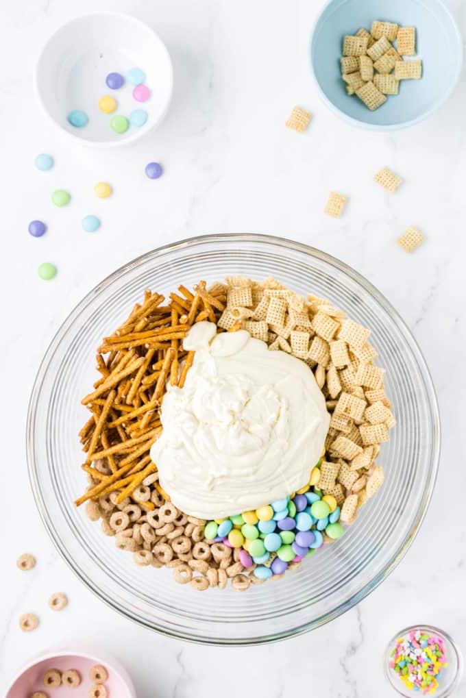 Ingredienti per 'Bunny Bait' in una ciotola di vetro trasparente circondata da una ciotola di codette, una ciotola con Cheerios, una ciotola di Chex di riso e una ciotola di M&M's