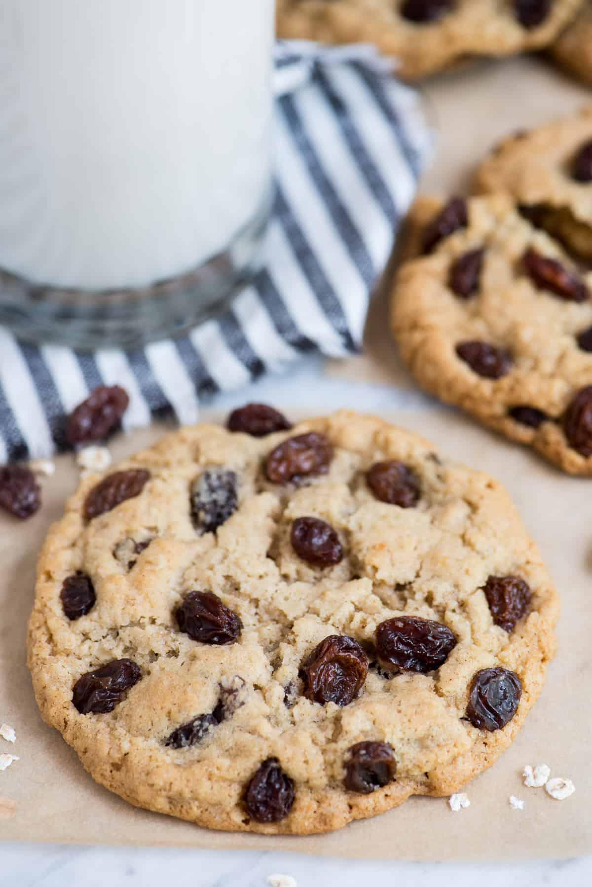 Biscotto avena e uvetta su carta forno marrone con un biscotto e un bicchiere di latte sullo sfondo