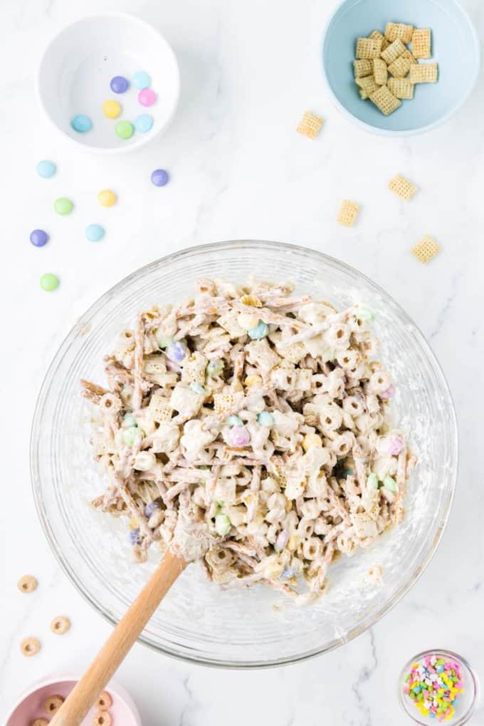 Snack mix 'Bunny Bait' in una ciotola di vetro trasparente circondata da una ciotola di codette, una ciotola con Cheerios, una ciotola di Chex di riso e una ciotola di M&M's