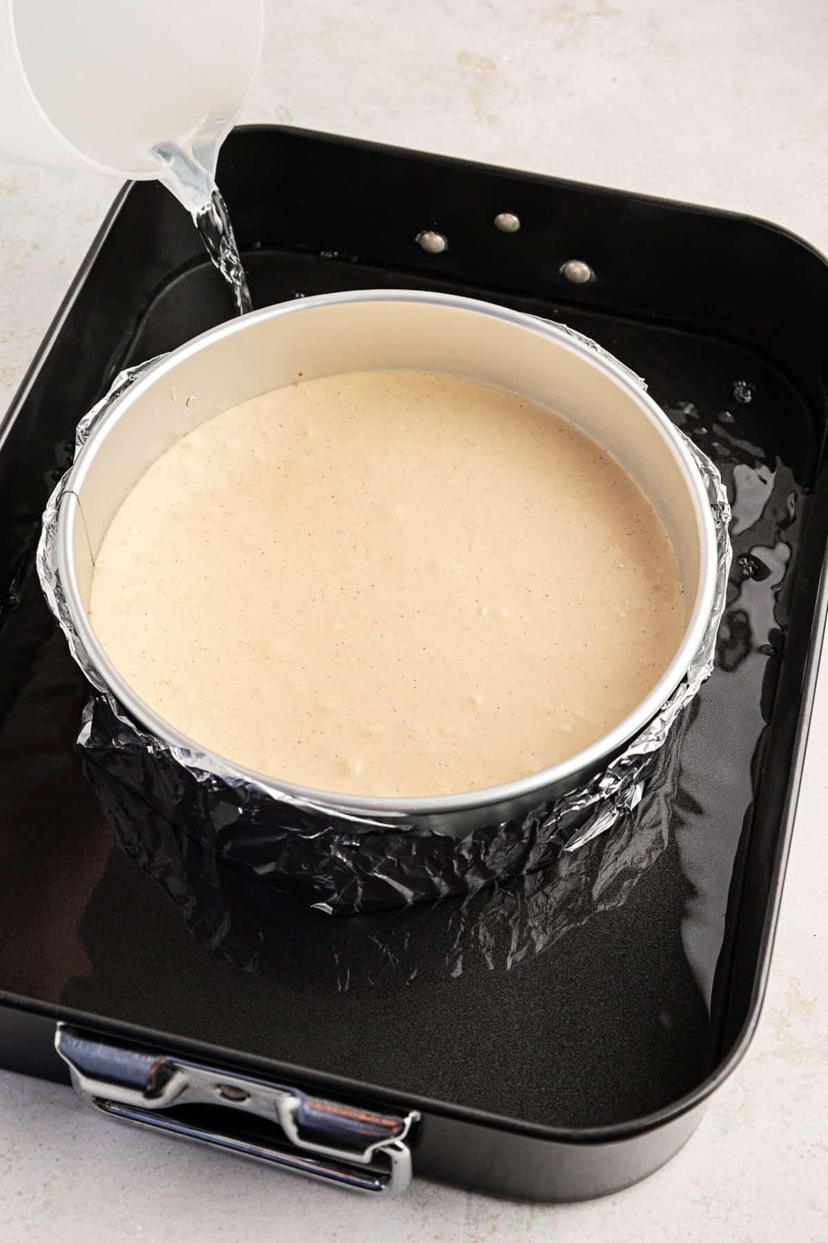 Impasto della cheesecake in una tortiera a cerniera circondata da acqua in una teglia da forno più grande