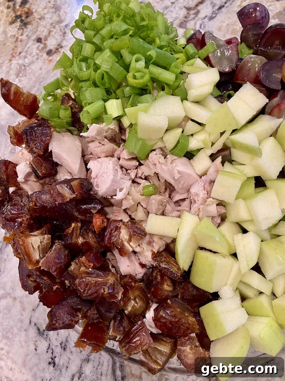 Chicken curry salad ingredients layered next to each other in a bowl.