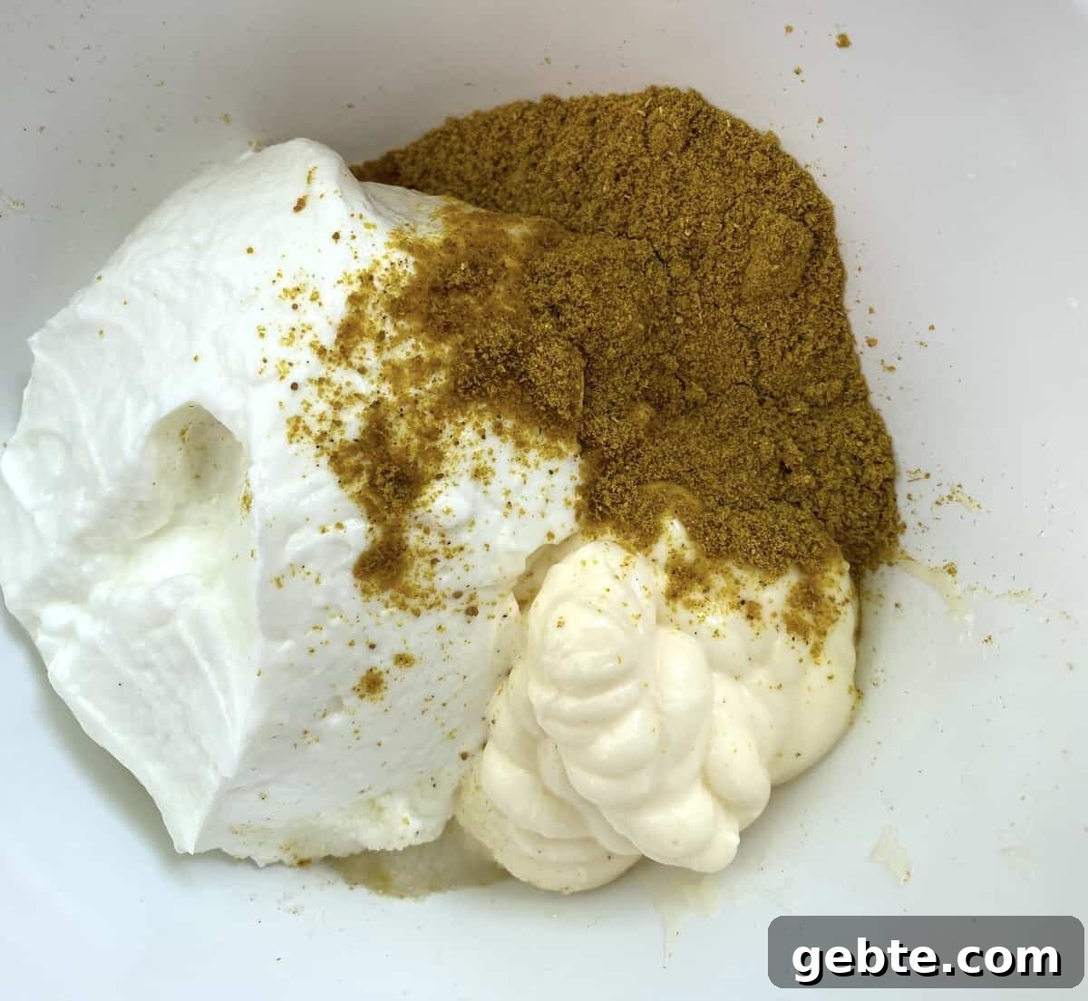 Curry powder on top of mayonnaise and non-fat Greek yogurt.