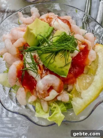 A small bowl of shrimp cocktail with lettuce, lemon, celery and avocado.